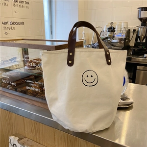 Close-up of canvas bucket bag with smiley face print and brown leather handles