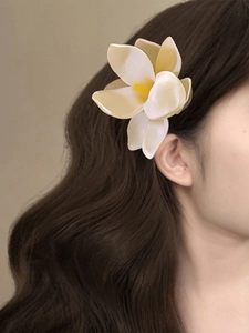 Frangipani fabric flower hair clip worn on side of wavy hair for vacation style