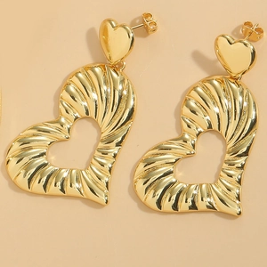 Detailed macro view of gold heart drop earrings featuring textured striped metal patterns