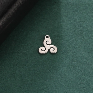 Polished stainless steel triskele pendant on a textured green background with leather