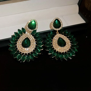 Macro detail of emerald waterdrop earrings with diamond accents and gold floral setting