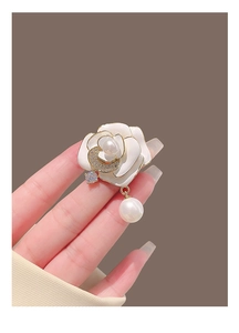 Gros plan détaillé d'une broche camélia blanc avec bord doré et pendentif en perle