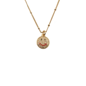 Gold smiling face pendant necklace with zircons and red enamel on white background