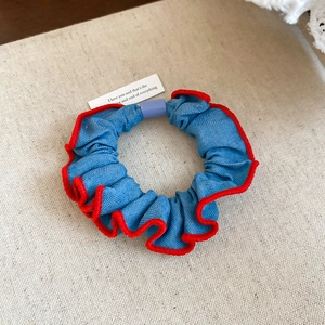 Close-up of blue denim scrunchie with red stitching detail on a canvas background