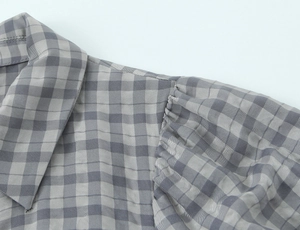 Detailed view of grey plaid dress featuring pleated shoulder accents and high collar texture