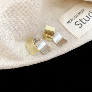 Macro view of gold and silver square stud earrings with polished metallic finish