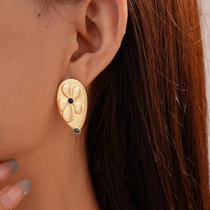Macro detail of a golden teardrop earring with matte finish and blue gemstone inlay