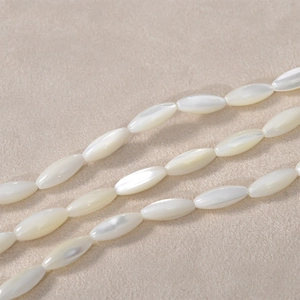 Macro shot of natural white shell rice-shaped beads with high luster on beige fabric texture