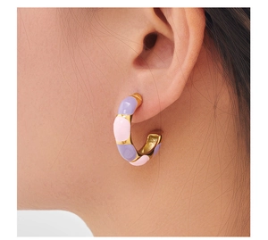 Close-up of gold C-shaped earrings with pink and purple enamel dots on a model's ear