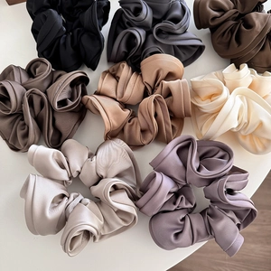 Flat lay of multiple satin silk scrunchies in cream, black, and champagne colors