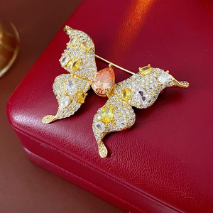Detail of gold butterfly brooch with orange pear-cut stones on a red leather jewelry box