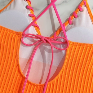 Macro detail of ribbed orange swimsuit with pink lace-up strings and silver eyelets