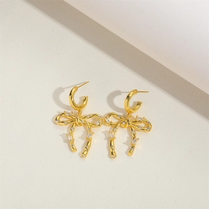 Elegant gold bow earrings with sparkling cubic zirconia set on a beige textured surface
