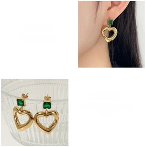 Detail view of gold heart pendants with emerald green square stones on models ear