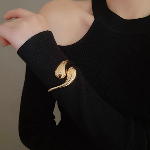 Polished gold liquid metal style open cuff bracelet worn over a black knit sleeve