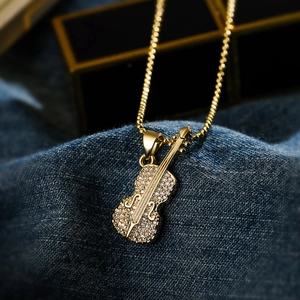 Gold plated guitar pendant necklace with sparkling cubic zirconia on blue denim fabric