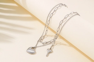 Detail of silver double-layer necklace with heart and key pendants on a textured background