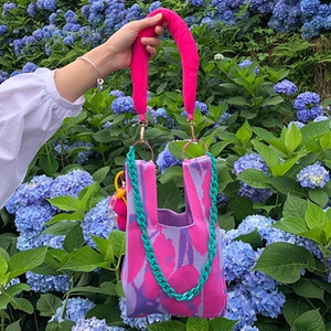 Detail of pink knitted tote bag featuring plush handles and green chain strap