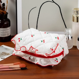 Détail de la trousse de maquillage cerise matelassée avec bords rouges sur table en bois