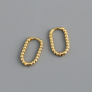 Detail of gold U-shaped oval hoop earrings with beaded texture on a grey background