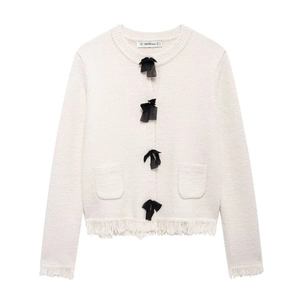 Detail of white knit cardigan showing black bow buttons and frayed tassel hem textures