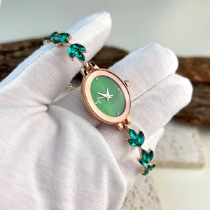 Detail of rose gold oval quartz watch with green dial and leaf-shaped gemstone links