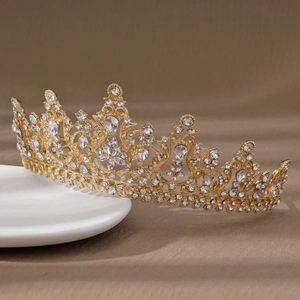 Elegant gold bridal crown with crystal leaf patterns resting on white ceramic tray