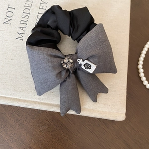Dettaglio scrunchie con fiocco in tessuto, ciondolo a camelia e cristallo su libri d'epoca