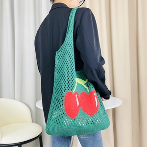 Close-up of green knitted tote bag with red cherry pattern worn by a model on shoulder