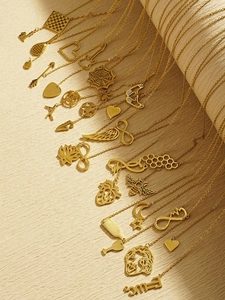 Close-up of golden stainless steel pendants with heart, arrow and bee motifs on paper
