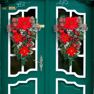 Pair of Christmas teardrop wreaths with red poinsettias and plaid bows on green doors