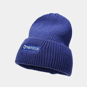 Close-up of dark blue knit beanie featuring white THE FOCUS logo on a stitched patch