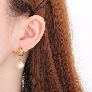 Close-up of matte gold geometric stud earrings featuring white circular pearls on model