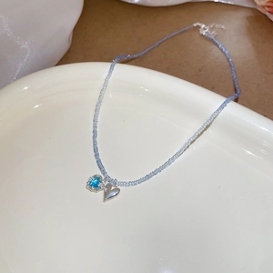 Detailed macro view of light blue beaded necklace with silver heart pendant on porcelain dish