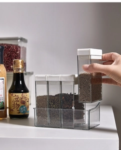 Hand picking a transparent seasoning jar from a four-piece kitchen spice box set with base