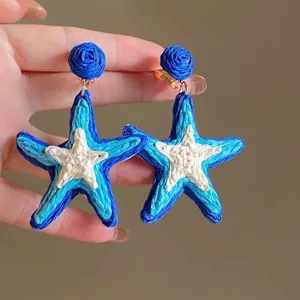 Detailed view of handmade woven starfish earrings in blue and cream colors