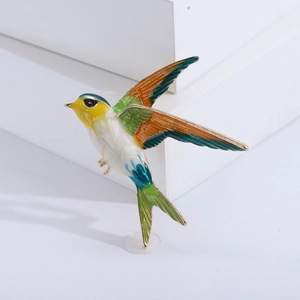 Macro detail of bird brooch with colorful enamel finish and gold metal frame on white backdrop