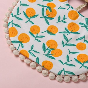 Gros plan du bavoir pour bébé avec motif orange, bordure à pompons et texture en coton