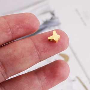 Polished golden butterfly metal bead pendant on fingertip for DIY jewelry making