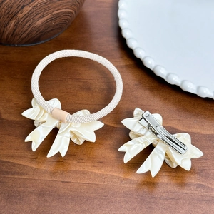 Elegant cream acetate bow hair clip and hair tie set on a minimalist wooden background