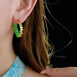 Détail de la boucle d'oreille créole dorée avec cristaux verts sur un modèle