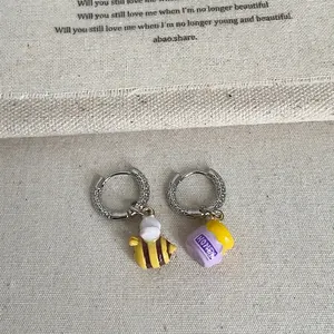 Asymmetric silver honeybee and honey jar charm hoop earrings on beige linen