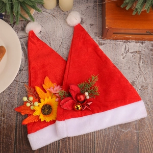 Two red plush Christmas hats with floral and pine decorations on snowy wood background