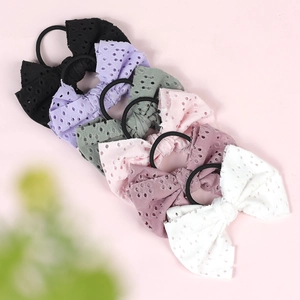 Detail of six textured bow hair ties in assorted soft colors on a pink background