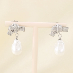 Detail of silver bow earrings with baroque pearl drops on a minimalist jewelry stand