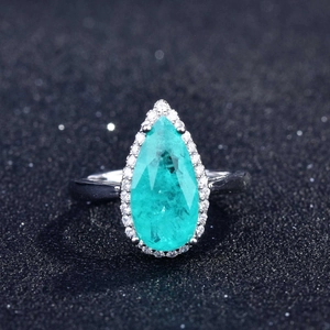Close-up of a pear-cut Paraiba tourmaline ring with halo setting on a black background