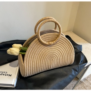 Close-up of beige woven half-moon straw handbag with round handles on a black surface