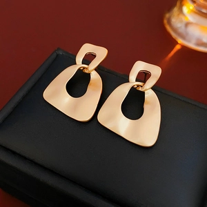 Close-up of matte gold geometric hollow earrings displayed on a black leather jewelry box