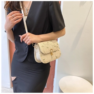Detailed close-up of beige straw crossbody bag with floral embroidery and white leather strap