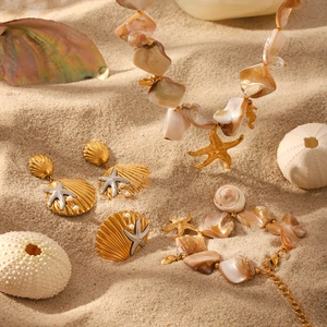 Golden starfish jewelry set with shells and pearls on sand background